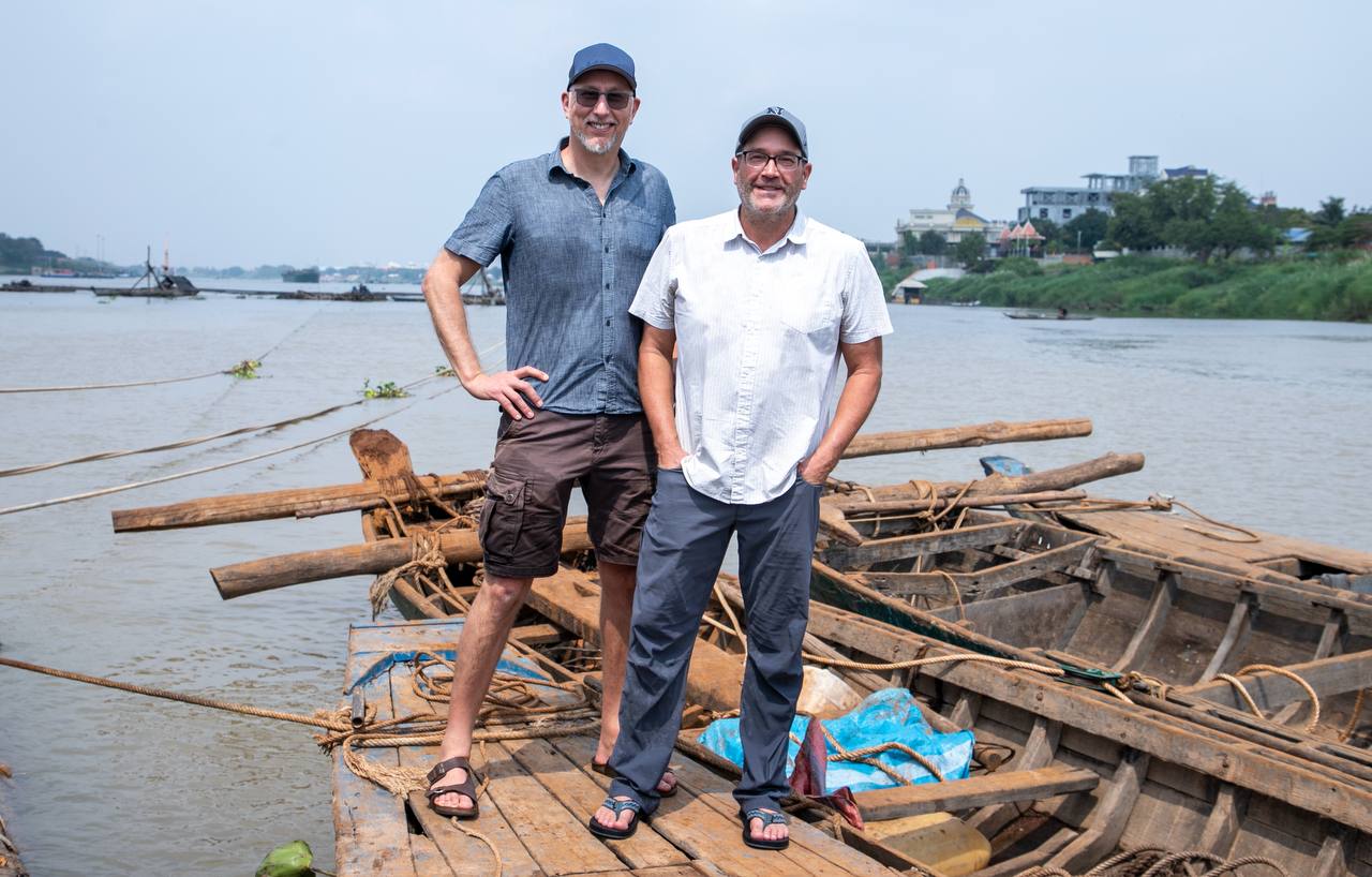 Stefan Lovgren and Zeb Hogan standing on fishing boats on the Mekong River
